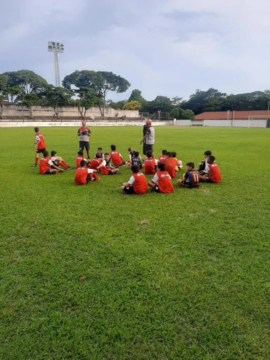 Treinador orientando um grupo de atletas sentado no campo.