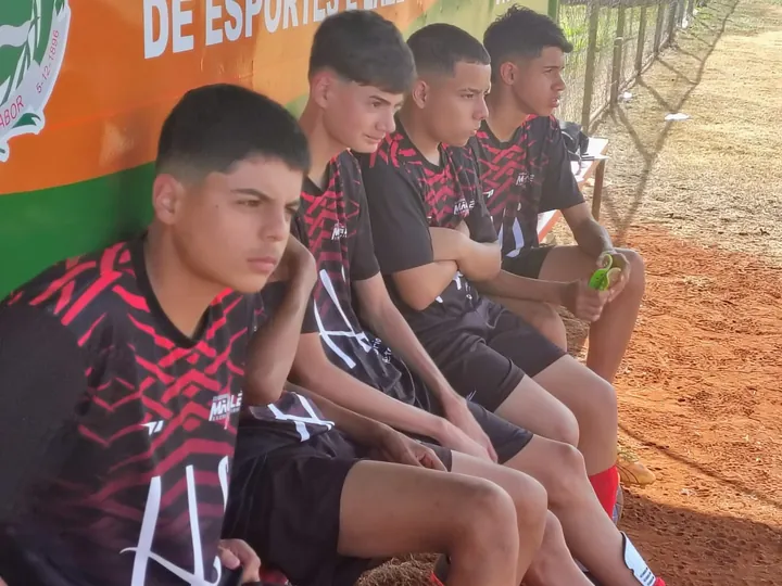 Atletas uniformizados sentados no banco à beira do campo.